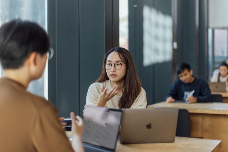 Two students in a discussion with their laptops open in front of them.
