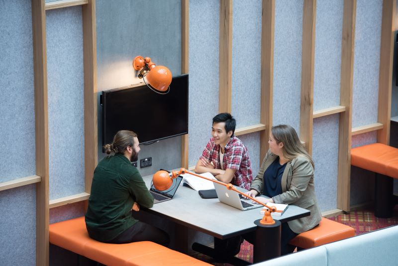 Three students seated at a table participating in a discussion.
