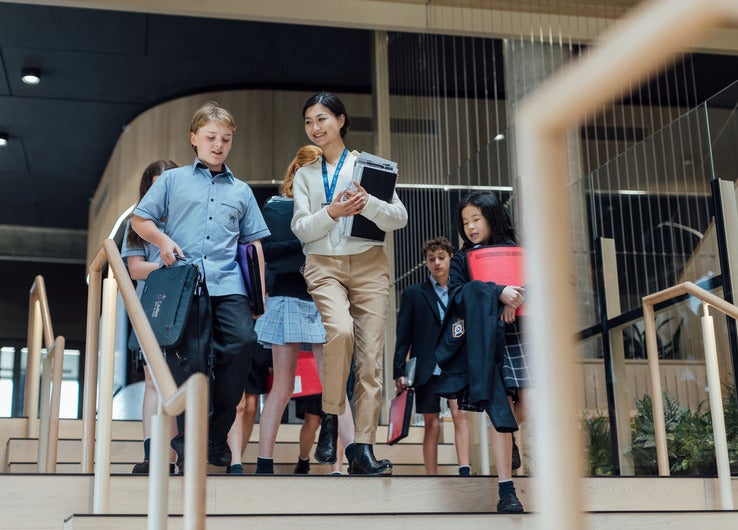 A group of students descending stairs in a school building, engaged in conversation with their teacher.