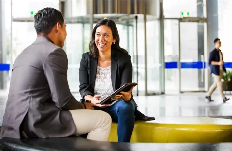 A woman speaking to a man in a relaxed setting of a lobby.