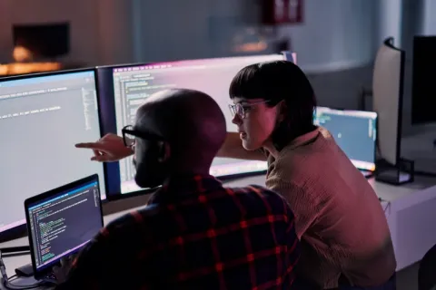 Two people analysing data on a computer screen, working together on cyber security solutions.