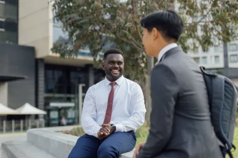 A student sitting near a garden on campus while another student walks by.