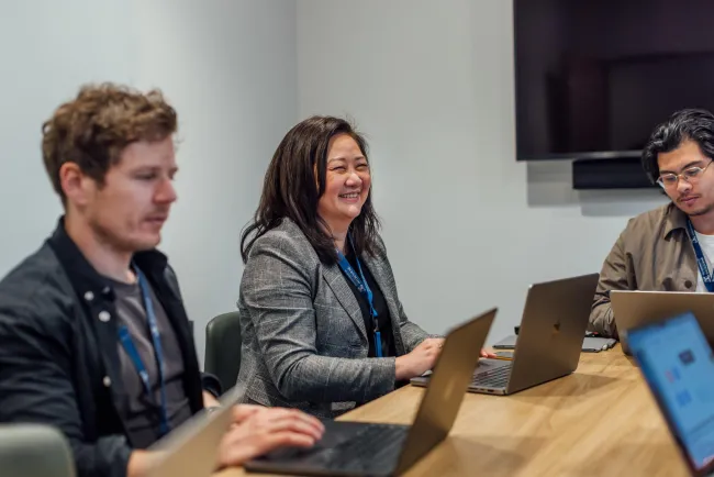 Three people sitting in a room with laptops open.
