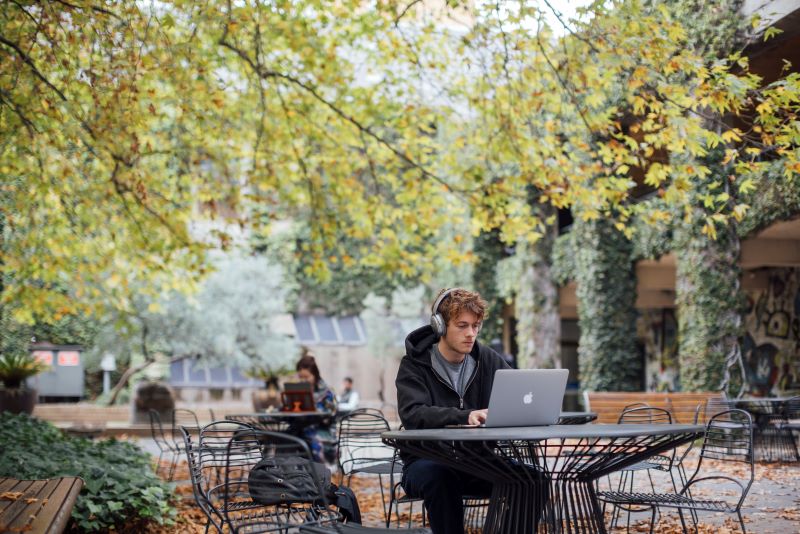 A man working on a laptop while sitting at a table in a park.