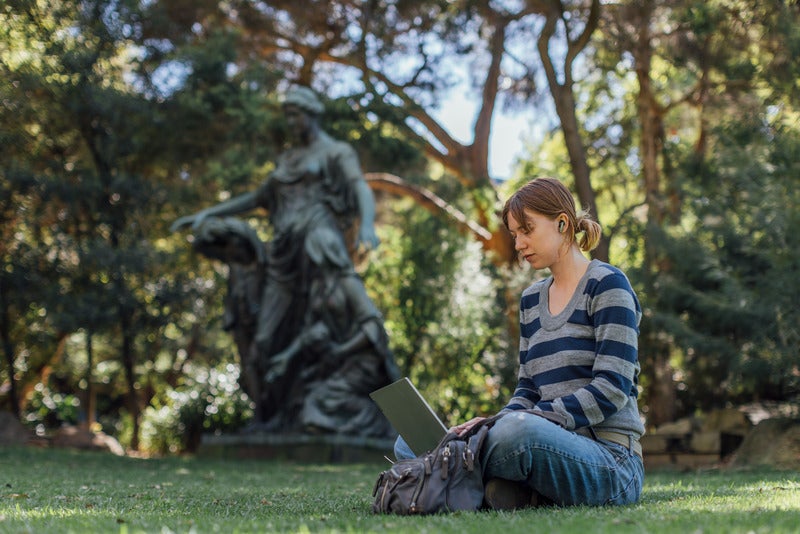 A woman sitting on grass with a laptop, engaged in work or study.