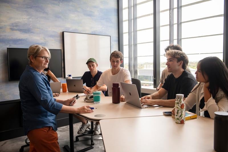  Several students seated at a table, engaged in discussion with an older professional.